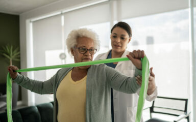 Physical therapist helping senior woman doing exercises with resistance band at home