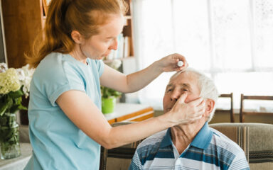 nurse putting drops into elderly senior man’s eyes