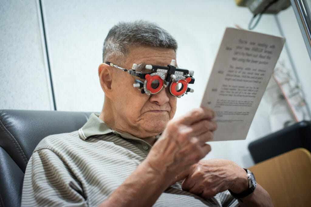 Optometrist using phoropter to check eyesight value for a senior man before making new eyeglasses in optical shop for eye care