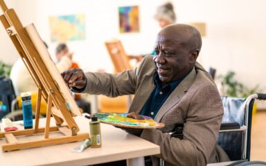 Happy retired man painting on canvas for art therapy