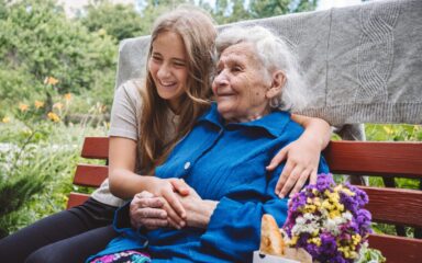 Grandparents Day, Reunited family, togetherness. Senior old grandma hugs granddaughter outdoors. Grandchild makes surprise for granny and gave her flowers