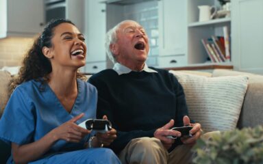 Shot of a young nurse sitting and bonding with her senior patient in the living room while playing video games