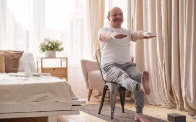 Elderly man practicing yoga asana or sport exercise for legs and hands on chair