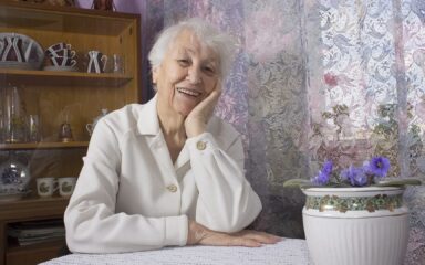 Old lonely woman sitting near the window in his house.