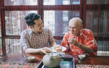 Chinese son sharing mooncake to his father during traditional mid-autumn festival at home during afternoon tea gathering