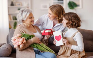 Happy International Mother’s Day.Smiling  daughter and granddaughter giving flowers  and gift to grandmother   celebrate spring holiday Women’s Day at home