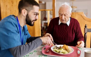 Male care worker serving dinner to a senior man at his home