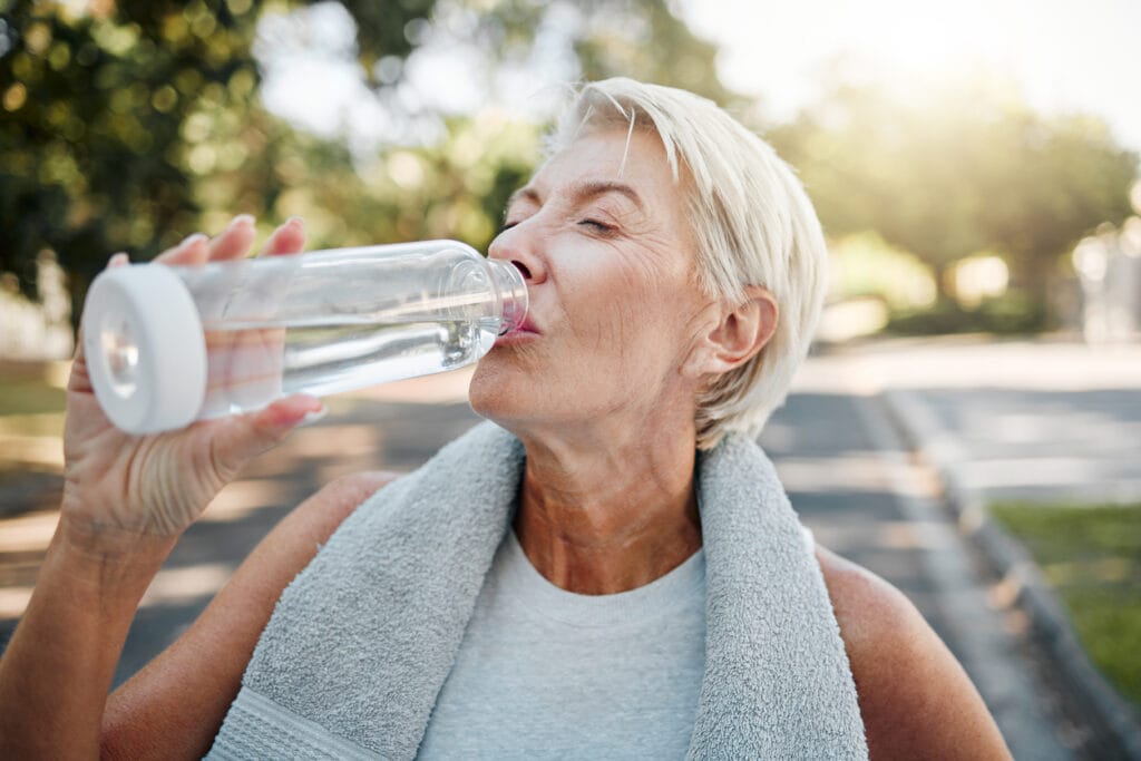 Senior fitness woman drinking water bottle outdoors after training