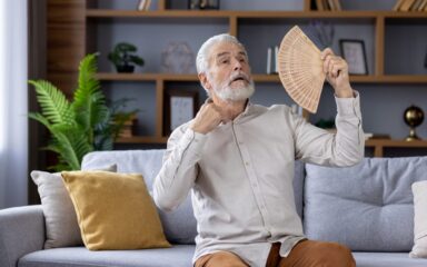 Senior man feeling hot and using fan on warm day at home