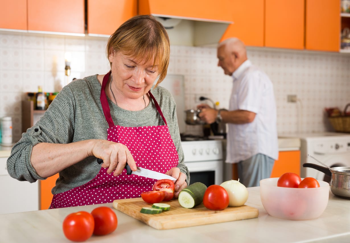 A senior couple cooking in a bright and cheery orange vintage looking kitchen to ensure they are Eating Right for Long-Term Health in Senior Years
