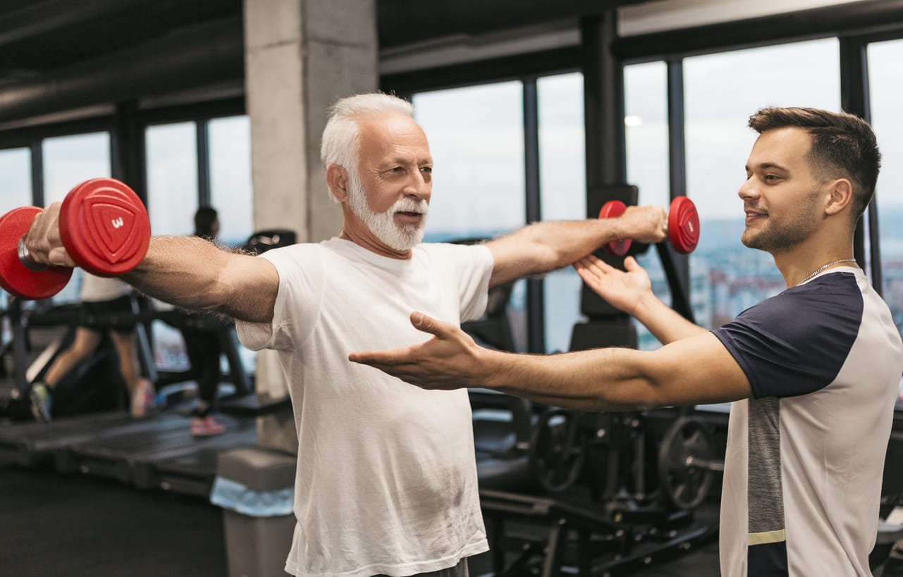 Balance-enhancing Exercises: Simple Exercises to Improve Strength and Balance. A senior man works with a trainer, performing strength exercises with light dumbbells to boost stability and muscle tone. Assisted Living Locators provides seniors with tips for easy, effective exercises to maintain balance and prevent falls.
