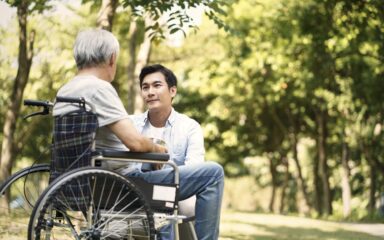 asian son consoling wheelchair bound father outdoors