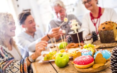 Tastu sugar coloured donuts on focus and happy family friends defocused in background during party celebration at home – concept of happiness and tradition together