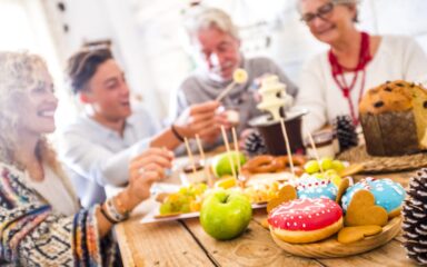 Tastu sugar coloured donuts on focus and happy family friends defocused in background during party celebration at home – concept of happiness and tradition together