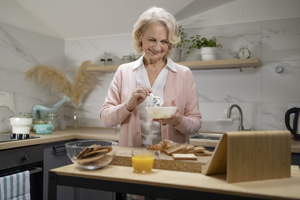 Senior Caucasian woman enjoying herself at home, chatting with her family using a digital tablet computer while preparing a breakfast in the kitchen and smiling. Essential Calcium Sources for Seniors