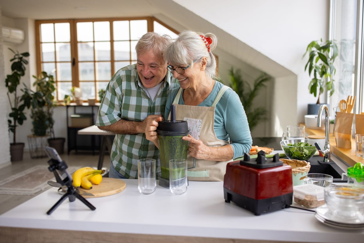 The Role of Fiber in Heart Health for Elderly Well-being. A joyful senior couple prepares a green smoothie, showcasing the importance of a fiber-rich diet in supporting heart health and overall wellness.