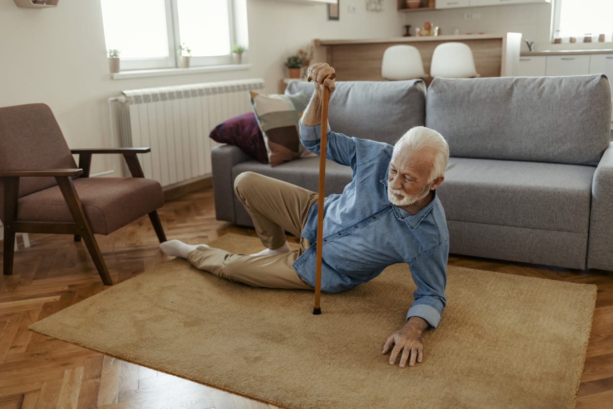 Assessing Home Hazards: How to Identify and Mitigate Common Household Fall Risks. An elderly man using a cane struggles to get up after a fall at home, highlighting the importance of creating a safe living environment. Assisted Living Locators offers tips to help families identify and reduce fall hazards in senior homes, ensuring greater safety and independence.